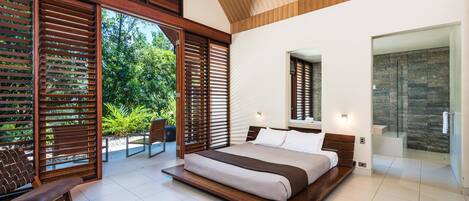 A modern bedroom with a large bed, wooden floor, and a view of greenery outside.