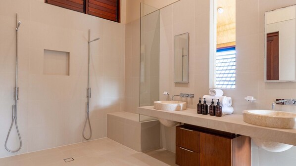Un baño moderno con cabina de ducha de vidrio, dos lavamanos y un tocador con espejo.