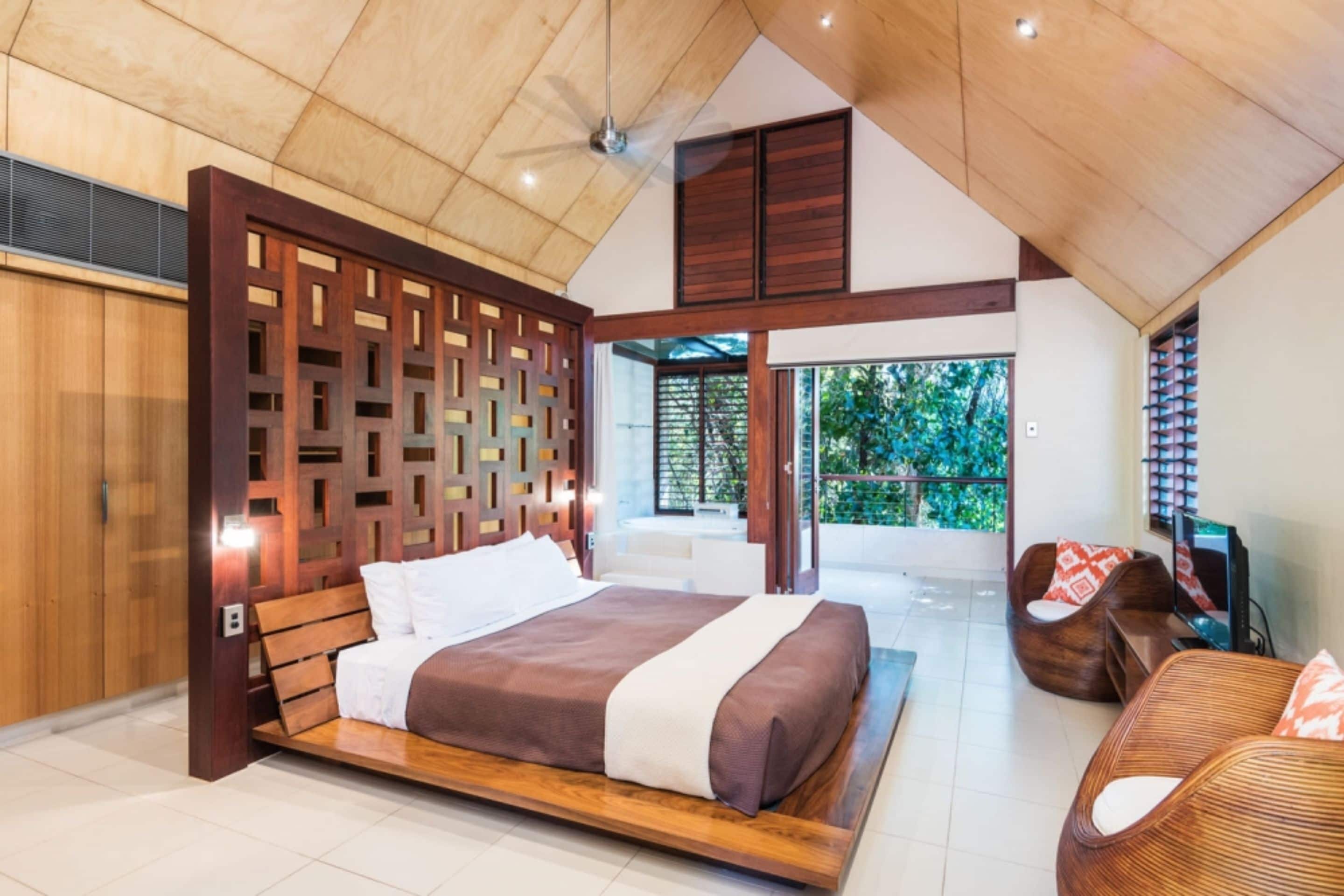 A spacious bedroom with a large bed, wooden headboard, and a view of greenery outside.