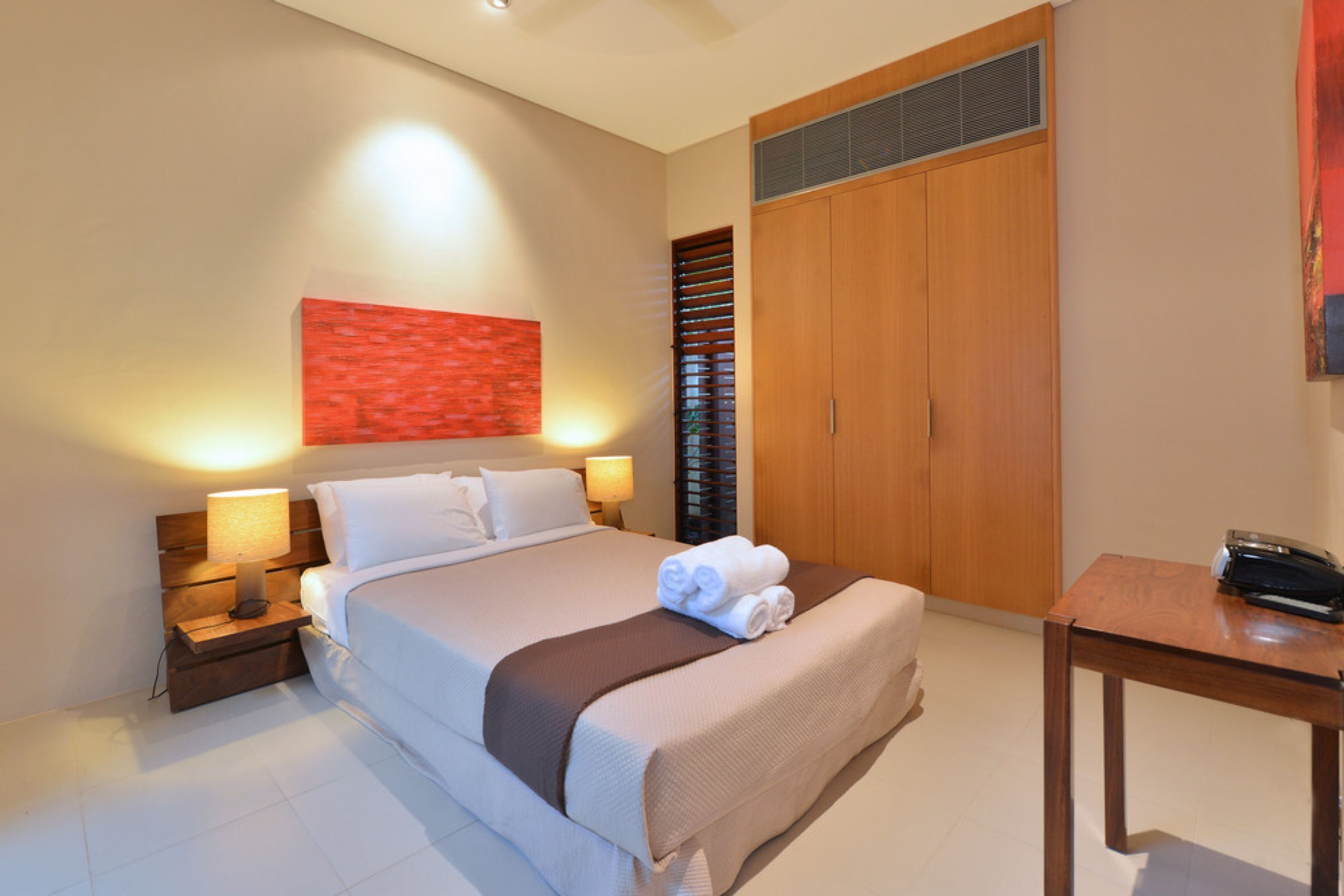 Une chambre d’hôtel avec un lit, des lampes de chevet, une armoire en bois et une petite table avec un téléphone.