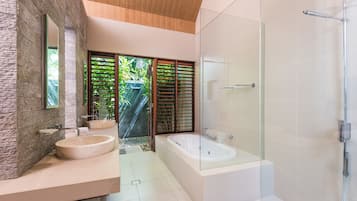 Une salle de bain moderne avec un mur en pierre, une grande baignoire et une douche séparée par une paroi de verre.