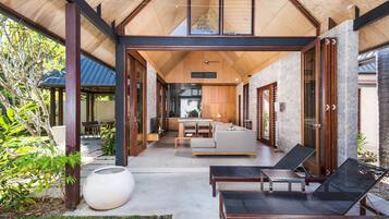 A modern outdoor living area with a wooden ceiling, a large white planter, and a seating arrangement including a sofa and two lounge chairs.