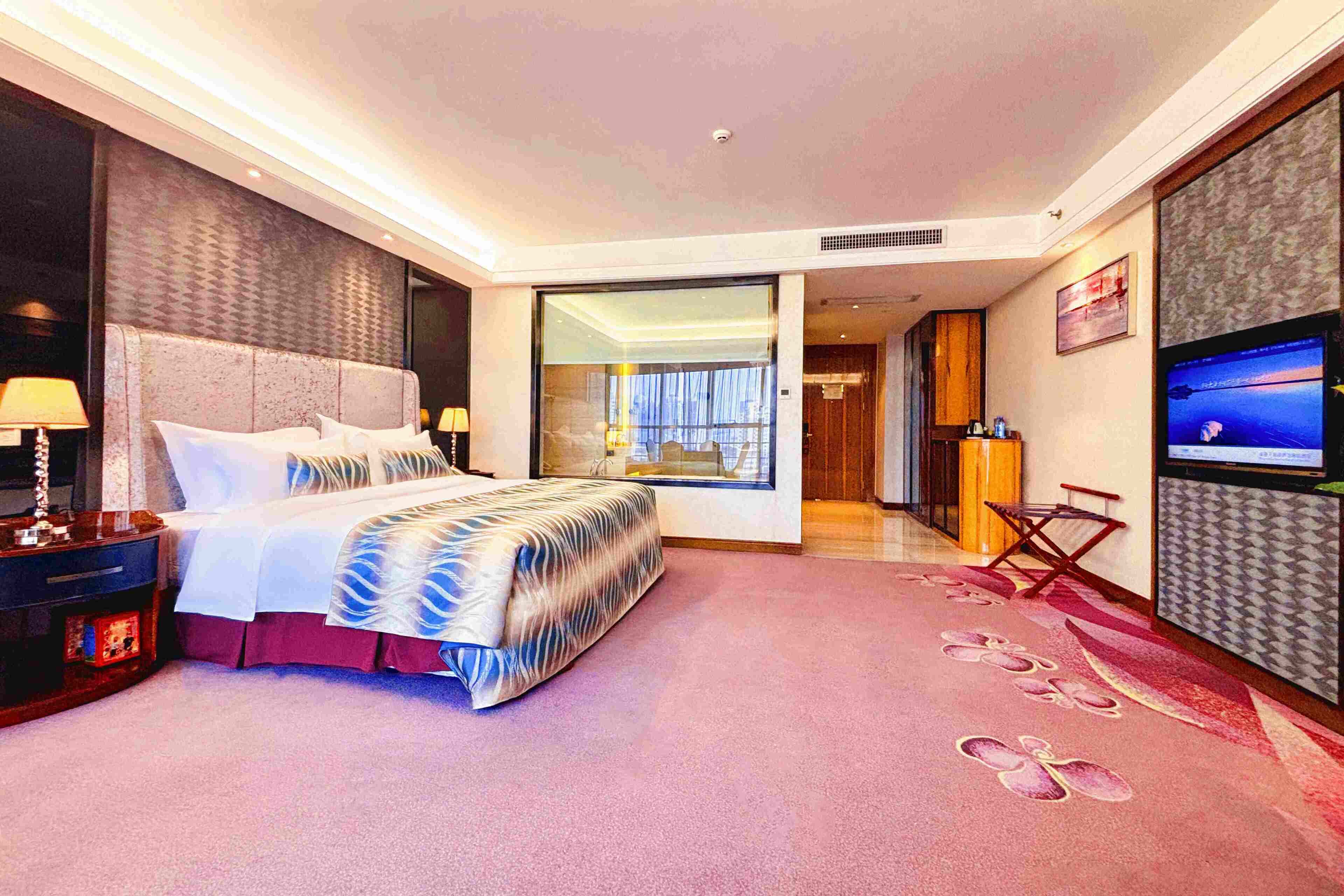 A modern hotel room with a large bed, a TV, a desk, and a view of the city.
