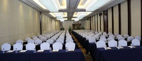 A conference room with rows of tables, white chairs, and a chandelier.