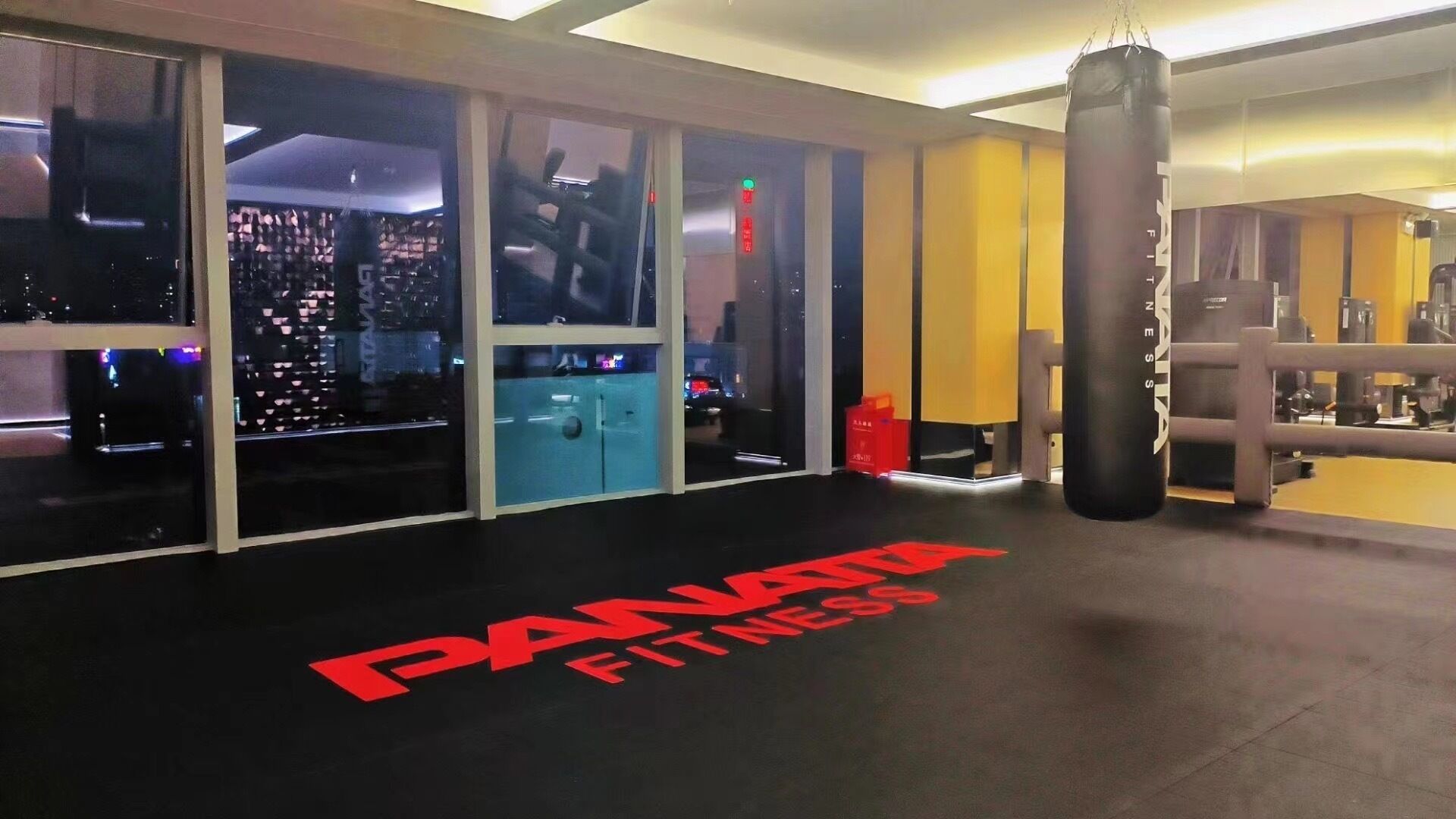 Et fitnesscenter med boksebold, træningsudstyr og store vinduer med udsigt over byen.