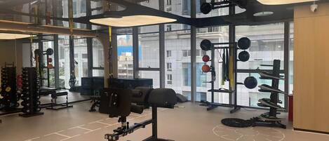 Ein modernes Fitnessstudio mit diversen Trainingsgeräten, großen Fenstern und einer hohen Decke.
