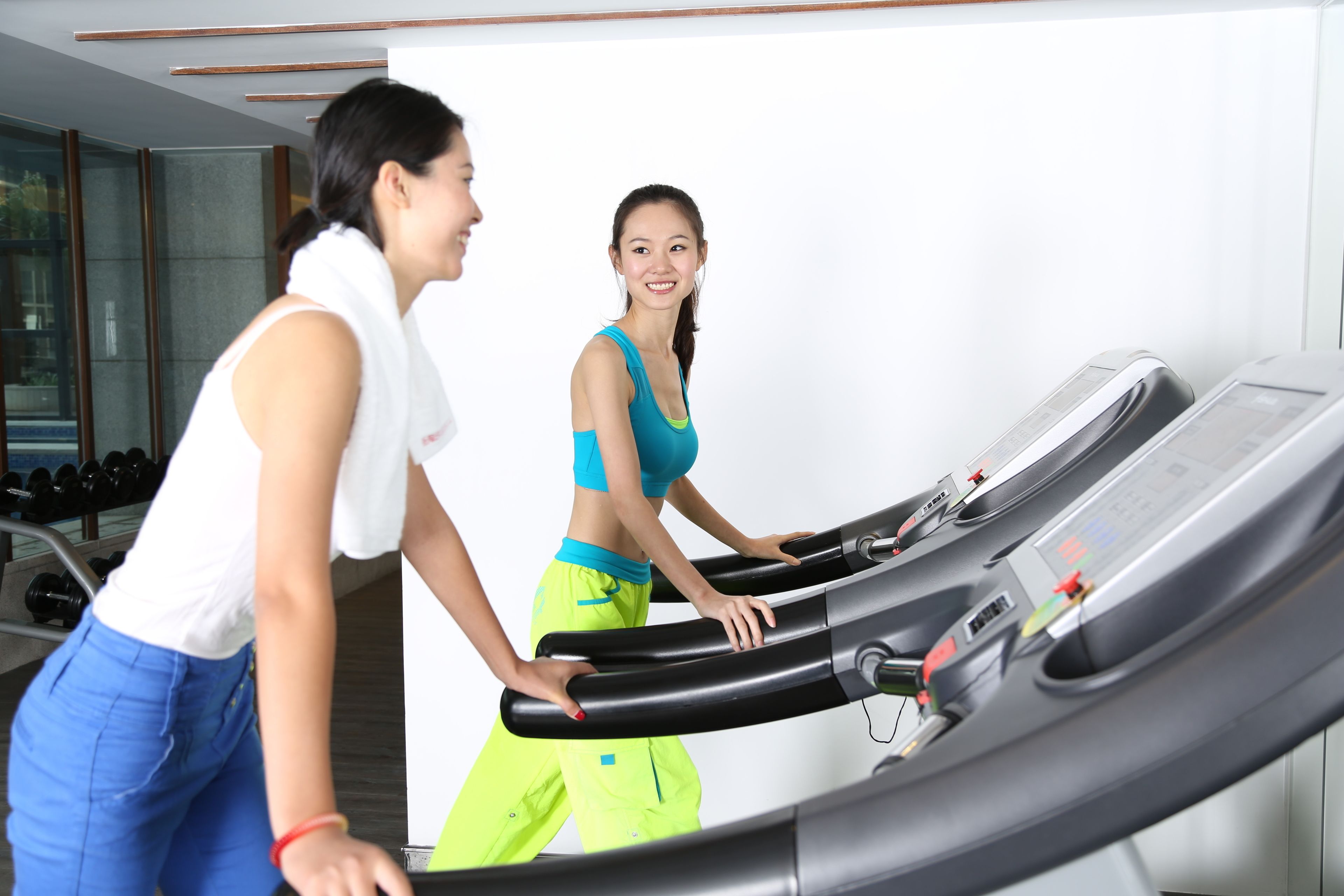 Two people on a treadmill in a gym with exercise equipment and a mirror on the wall.