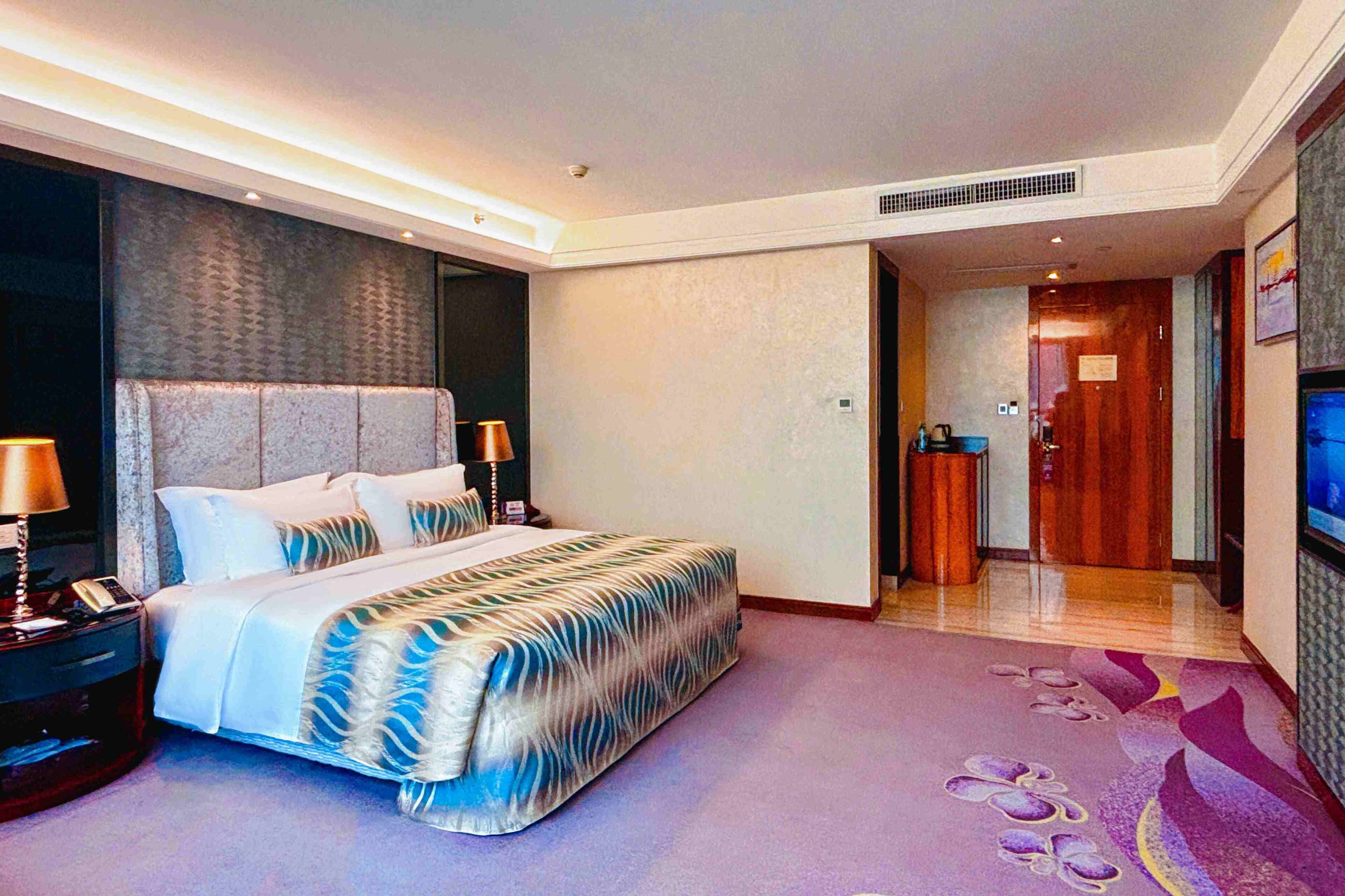 A hotel room with a large bed, bedside tables, a TV, and a bathroom visible through an open door.