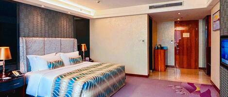 A hotel room with a large bed, bedside tables, a TV, and a bathroom visible through an open door.