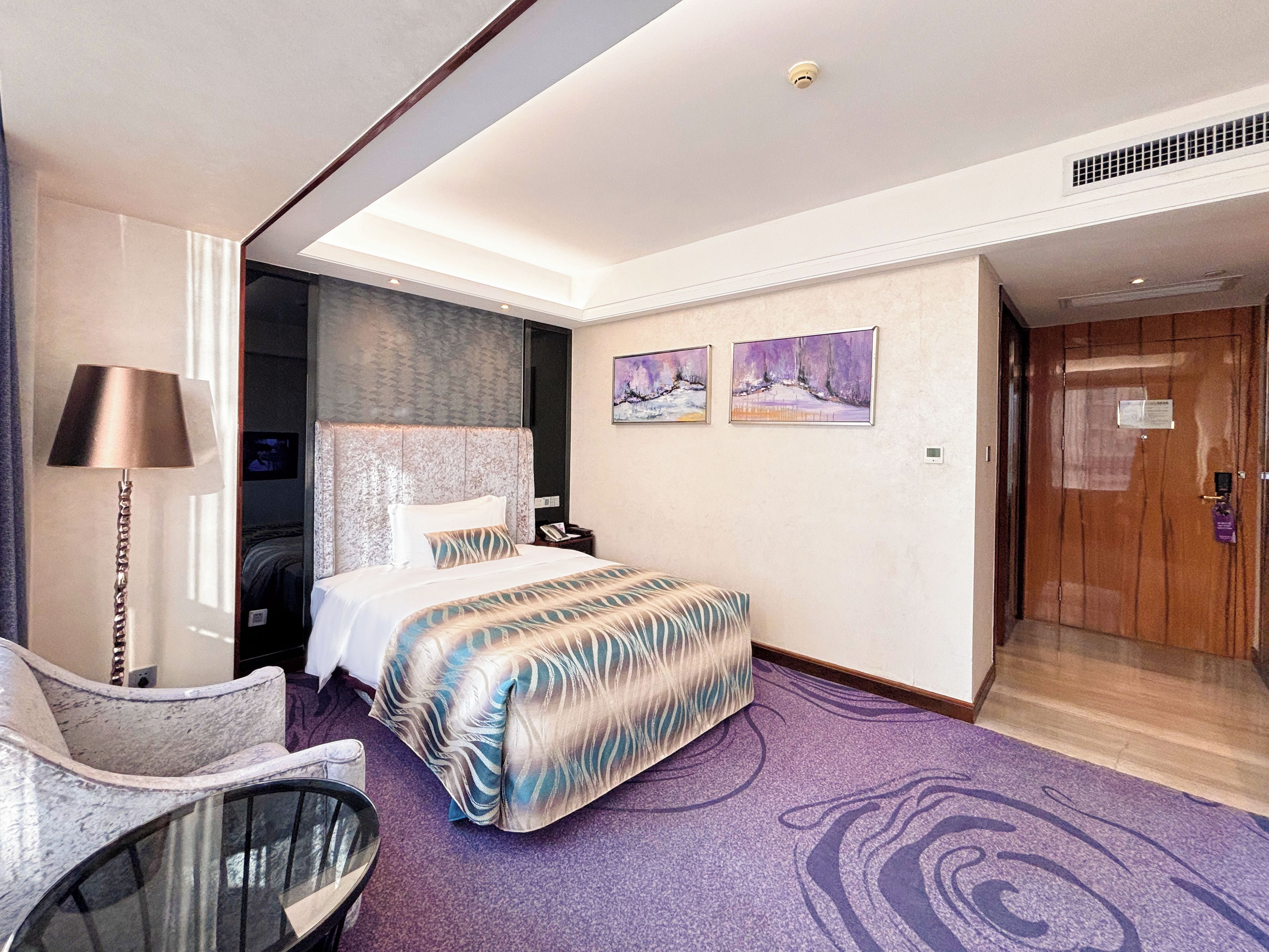 A hotel room with a bed, a chair, a small table, and a door.