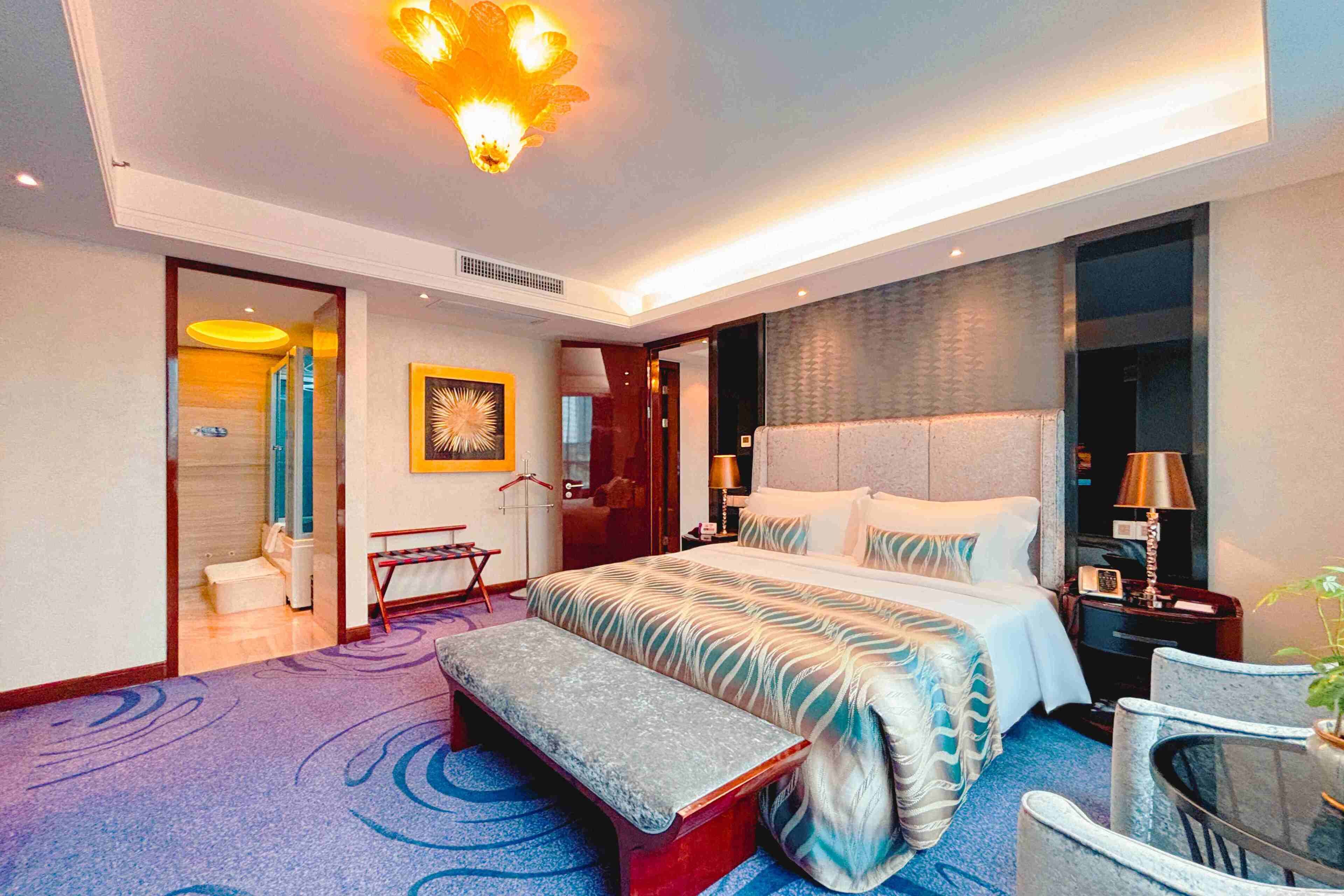 Una habitación de hotel moderna con una cama grande, un banco, una mesita pequeña y una silla.