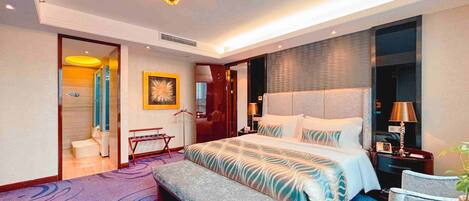 Una habitación de hotel moderna con una cama grande, un banco, una mesita pequeña y una silla.