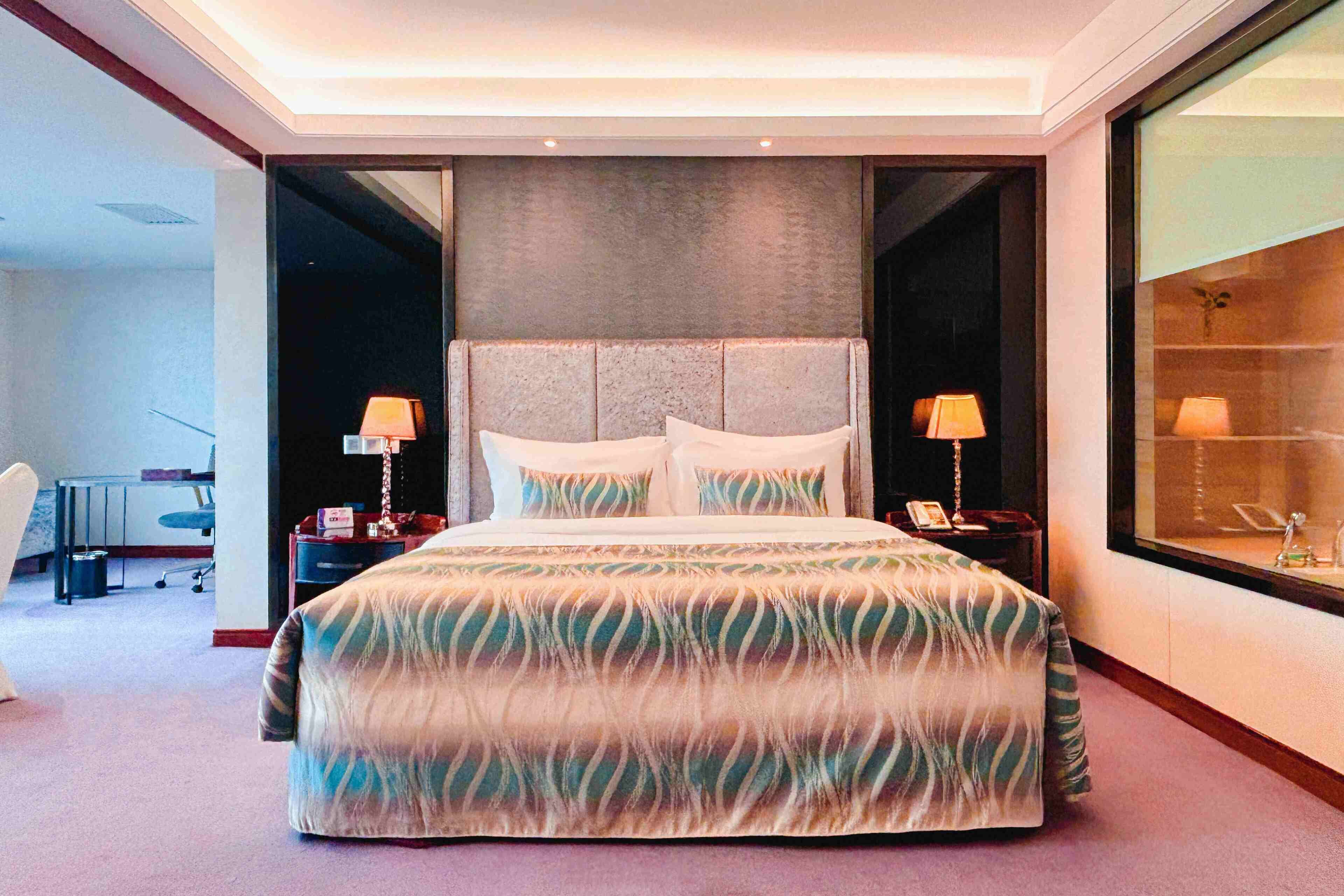 Un grand lit recouvert d’une couvre-lit à motifs, deux lampes de chevet et une vue sur l’extérieur grâce à une grande fenêtre.