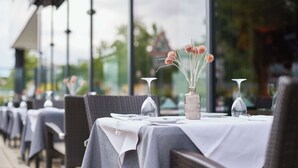 Un restaurante con mesas dispuestas para comer, con mantel blanco y un jarrón con flores secas.
