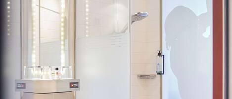 A modern bathroom with a glass-enclosed shower, a large mirror with lights, and a vanity with a sink and towel rack.