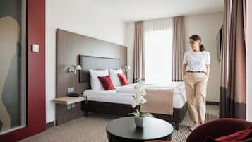 A hotel room with a bed, bedside table, lamp, and a small table with a flower.