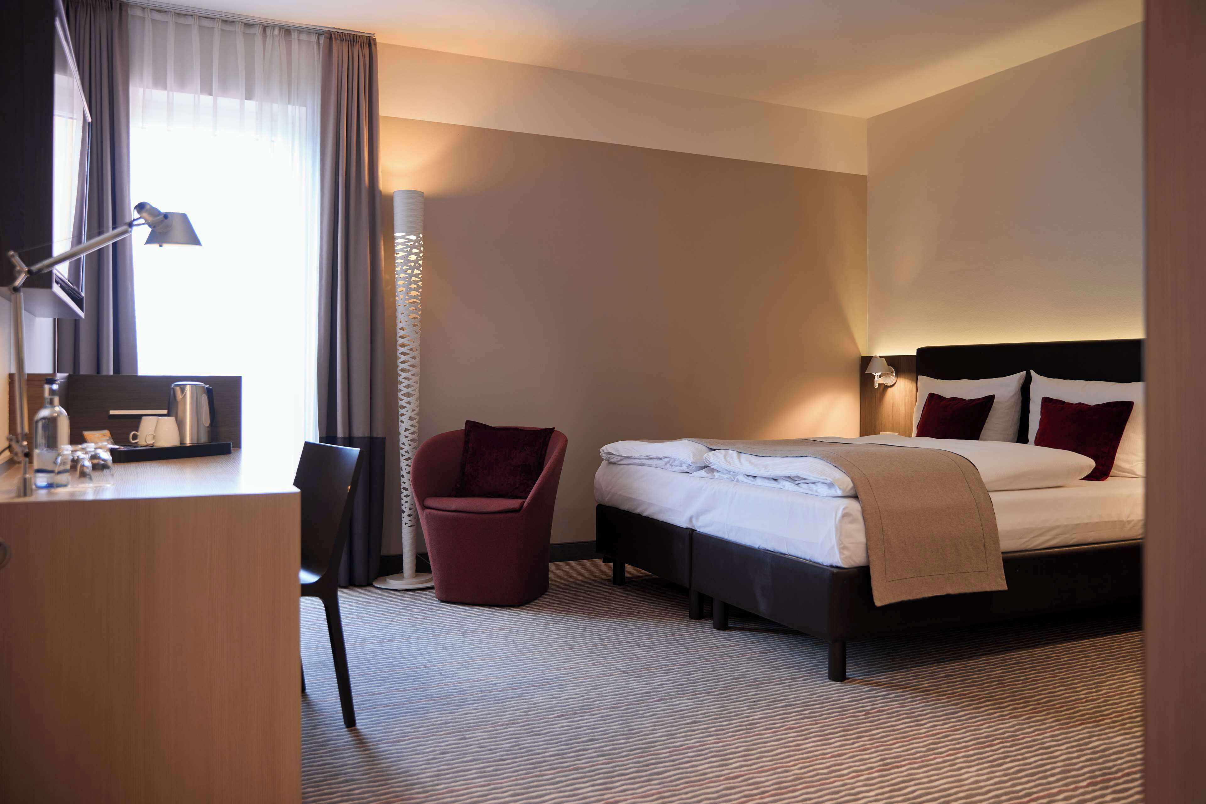 A hotel room with a bed, a desk, a chair, and a lamp.