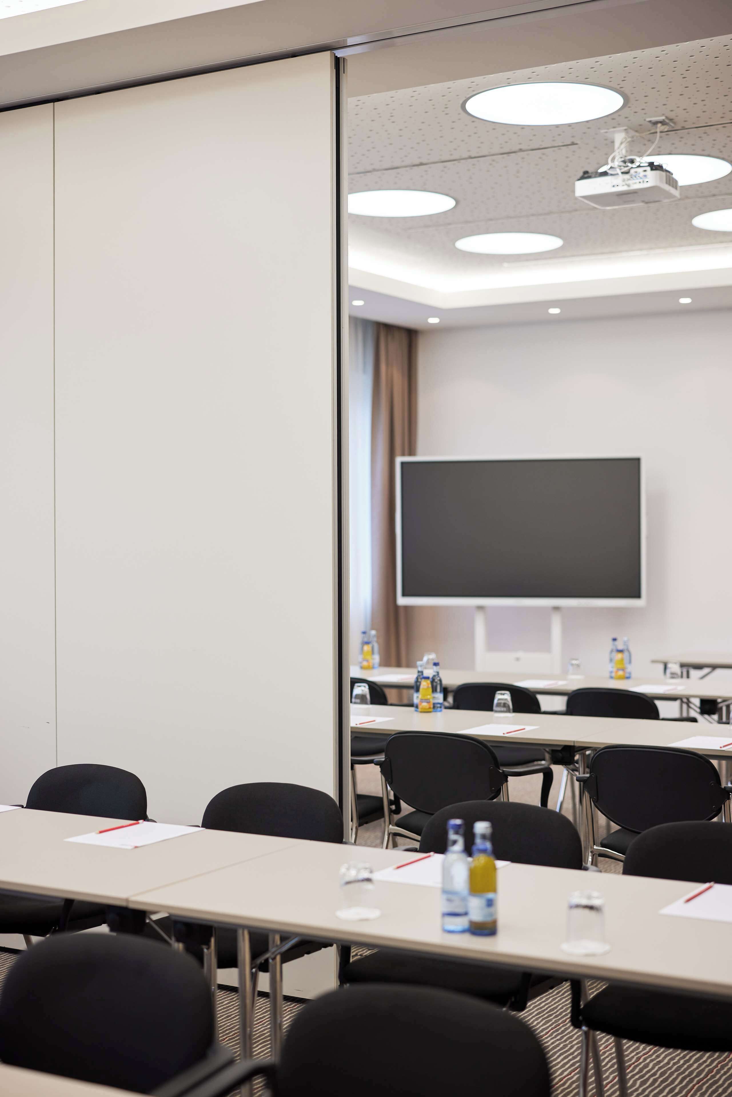 A conference room with a large flat-screen TV, multiple tables, chairs, and ceiling lights.