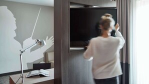 Una habitación de hotel moderna con un televisor de pantalla plana grande montado en una pared de madera, un escritorio con una lámpara y un libro.