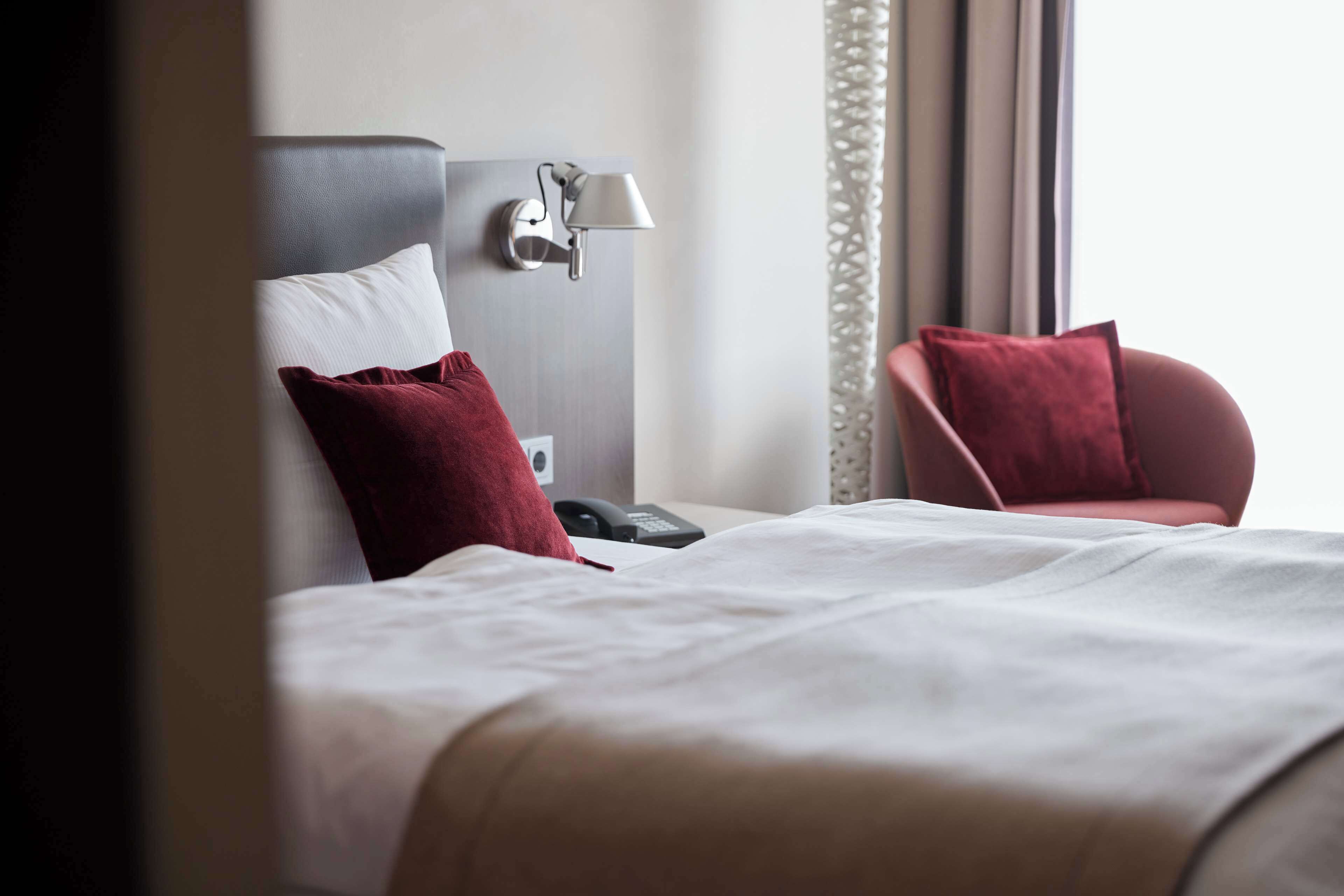 A hotel room with a bed, a bedside table with a lamp, a phone, and a chair.