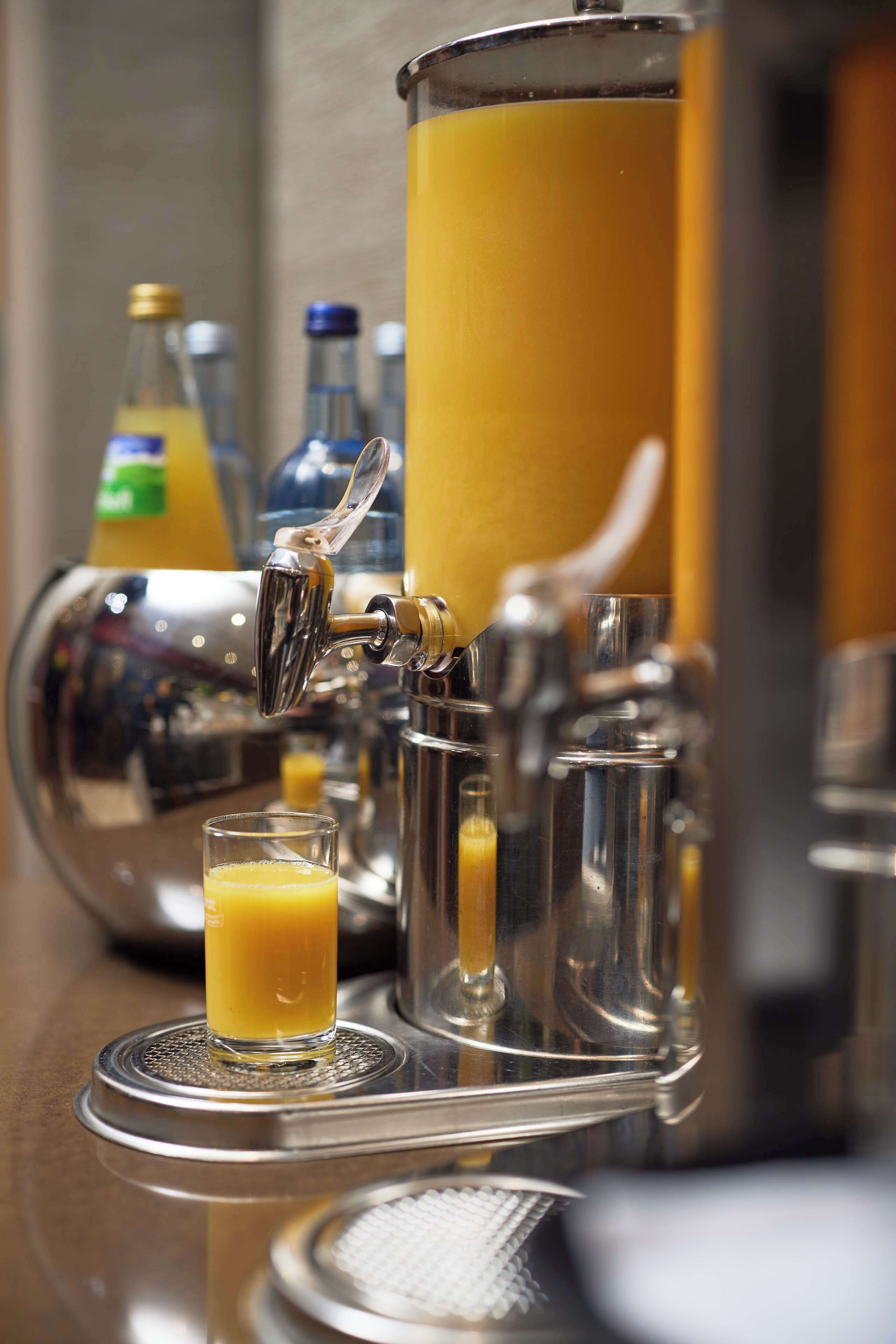 A barista station with a coffee machine, a milk frother, and a glass of orange juice.