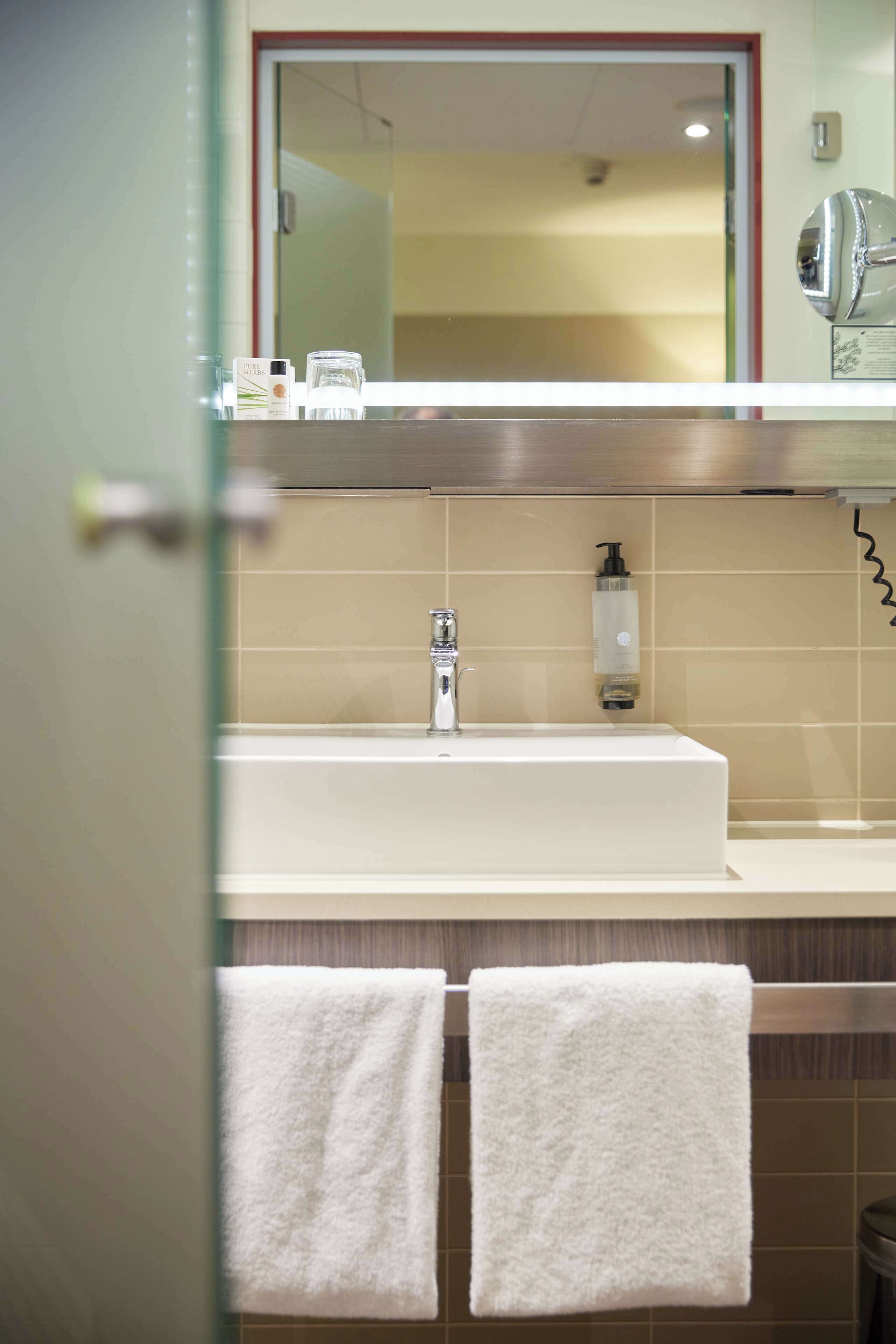 Ein Badezimmer mit einem weißen Waschbecken, einem Spiegel darüber und zwei weißen Handtüchern an einem Haken.