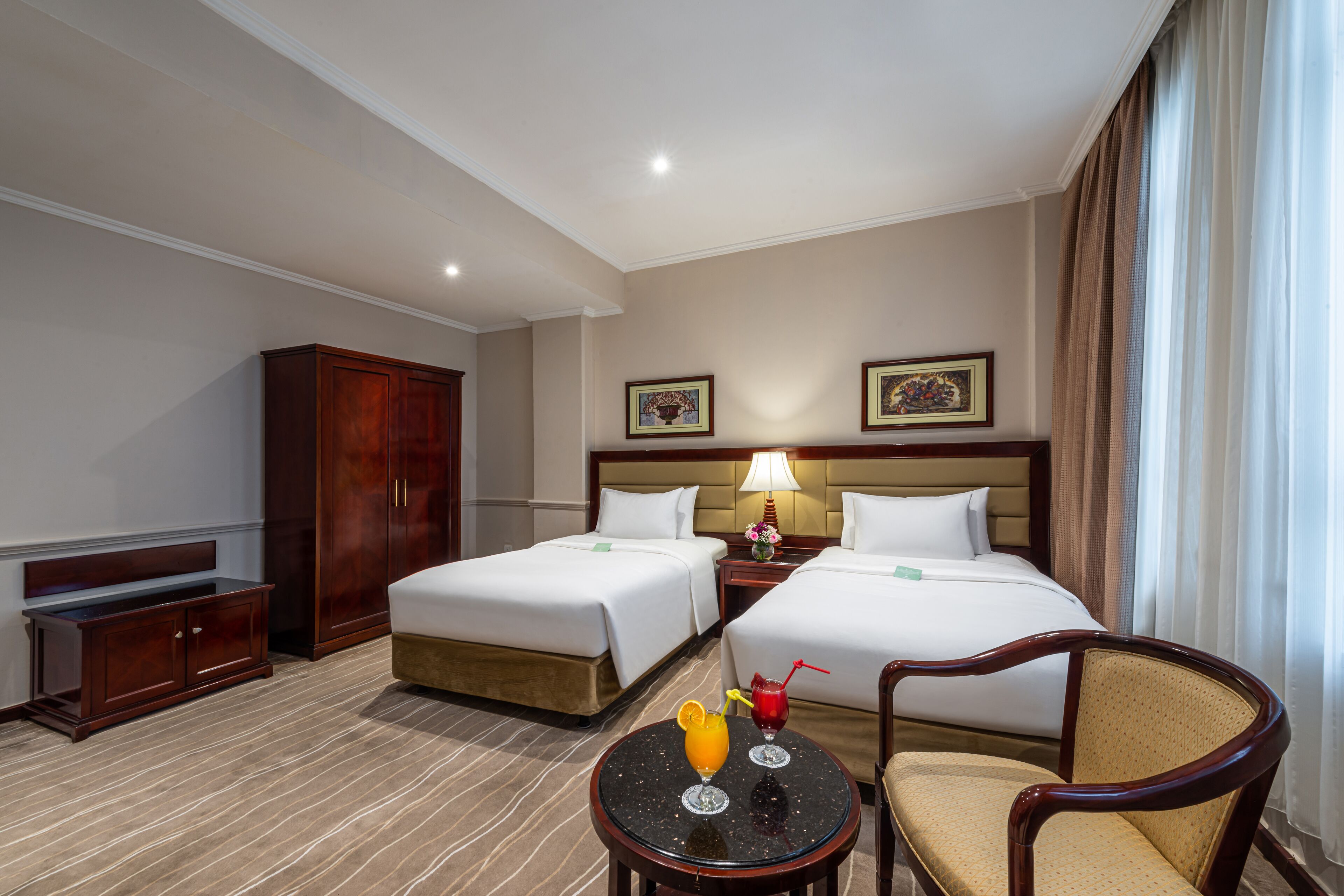 Habitación de hotel con dos camas, un escritorio, una silla y una mesita con bebidas.