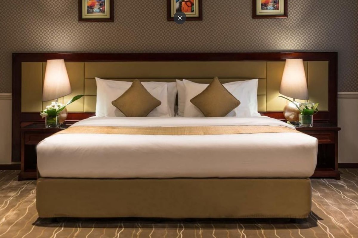 Una habitación de hotel con una cama grande, dos mesitas de noche y un cabecero.