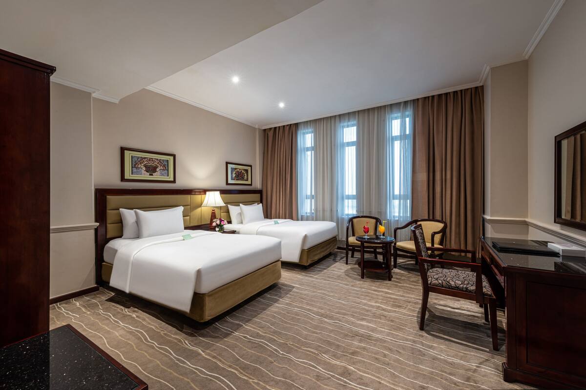 A hotel room with two beds, a desk, a chair, and a large window with curtains.
