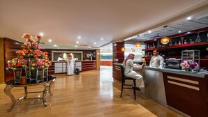 A hotel lobby with a reception desk, a glass-top table with floral arrangements, and a bar area with shelves of bottles. - Boudl Abha (Abha)