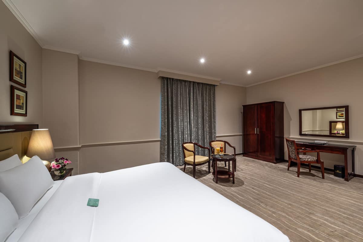 A hotel room with a large bed, two chairs, a desk, a lamp, and a mirror.