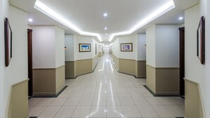 A long, well-lit hallway with a tiled floor, framed pictures on the walls, and doors on both sides. - Boudl Abha (Abha)