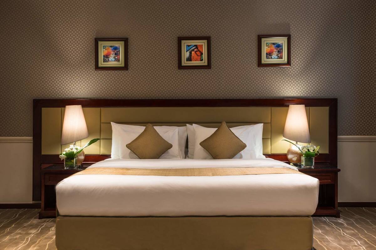 A hotel room with a large bed, two bedside lamps, and three framed artworks on the wall.