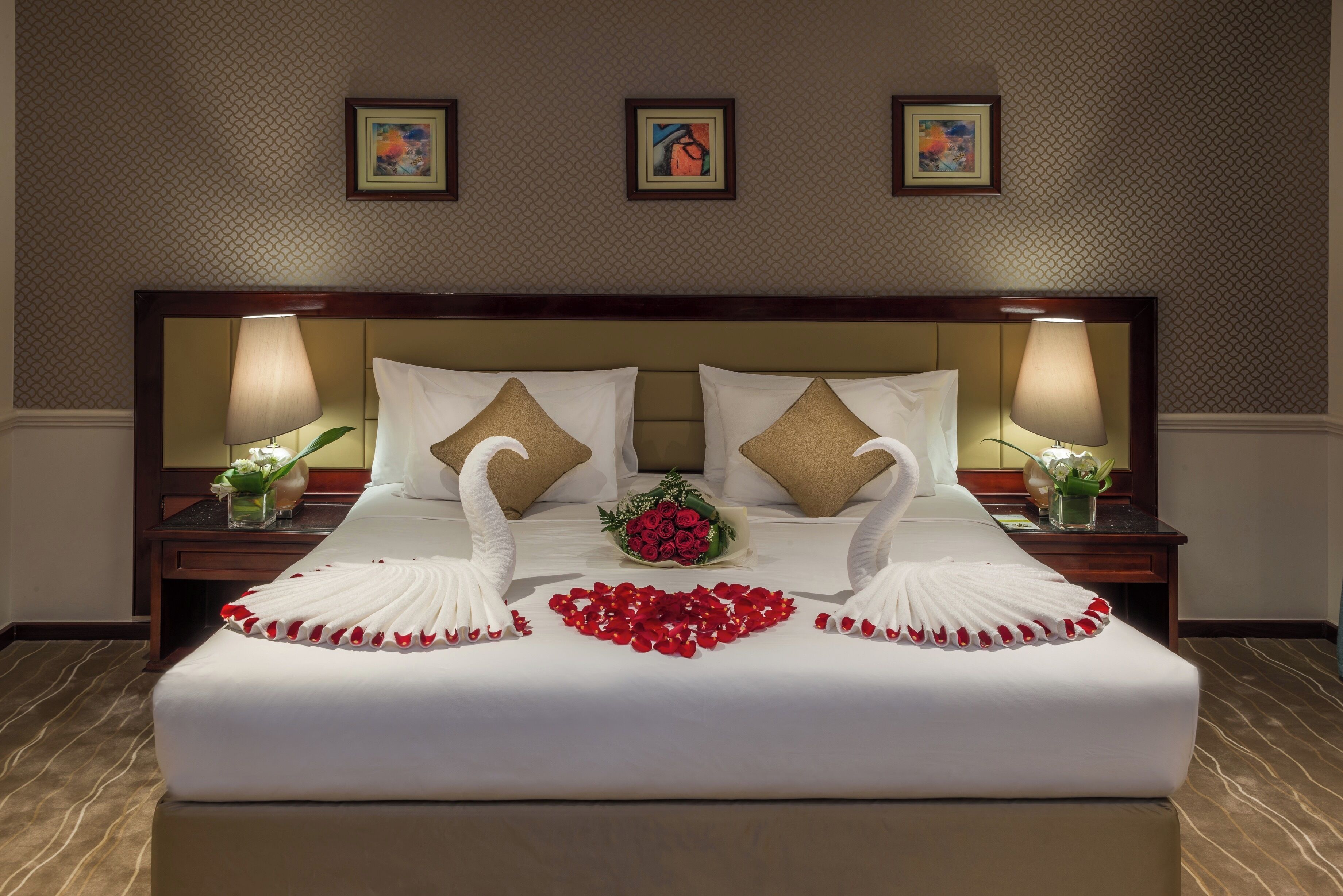 Ein Hotelzimmer mit einem ordentlich bezogenem Bett, einem Strauß roter Rosen und zwei schwanenförmigen Kissen.