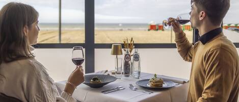 A dining table with a view of the beach, a candle, and a bottle of water.
