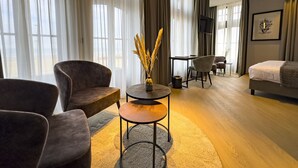 Una habitación de hotel moderna con sofá, sillón, mesa redonda y cama.