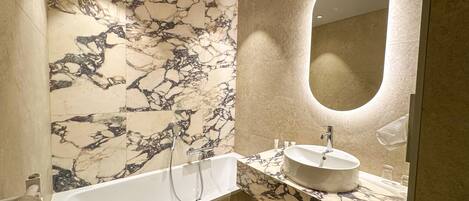 Un baño moderno con pared de mármol, una bañera independiente, un lavamanos con encimera de mármol y un espejo grande.