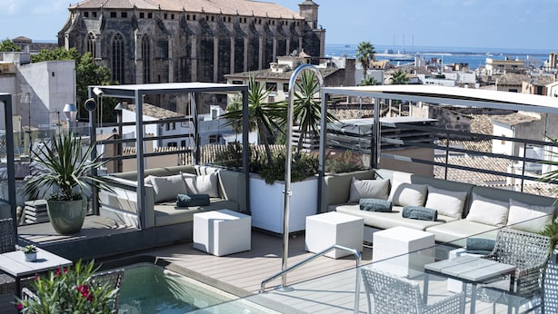 Une terrasse sur le toit avec une piscine, des espaces de détente en plein air et une vue sur un bâtiment historique.