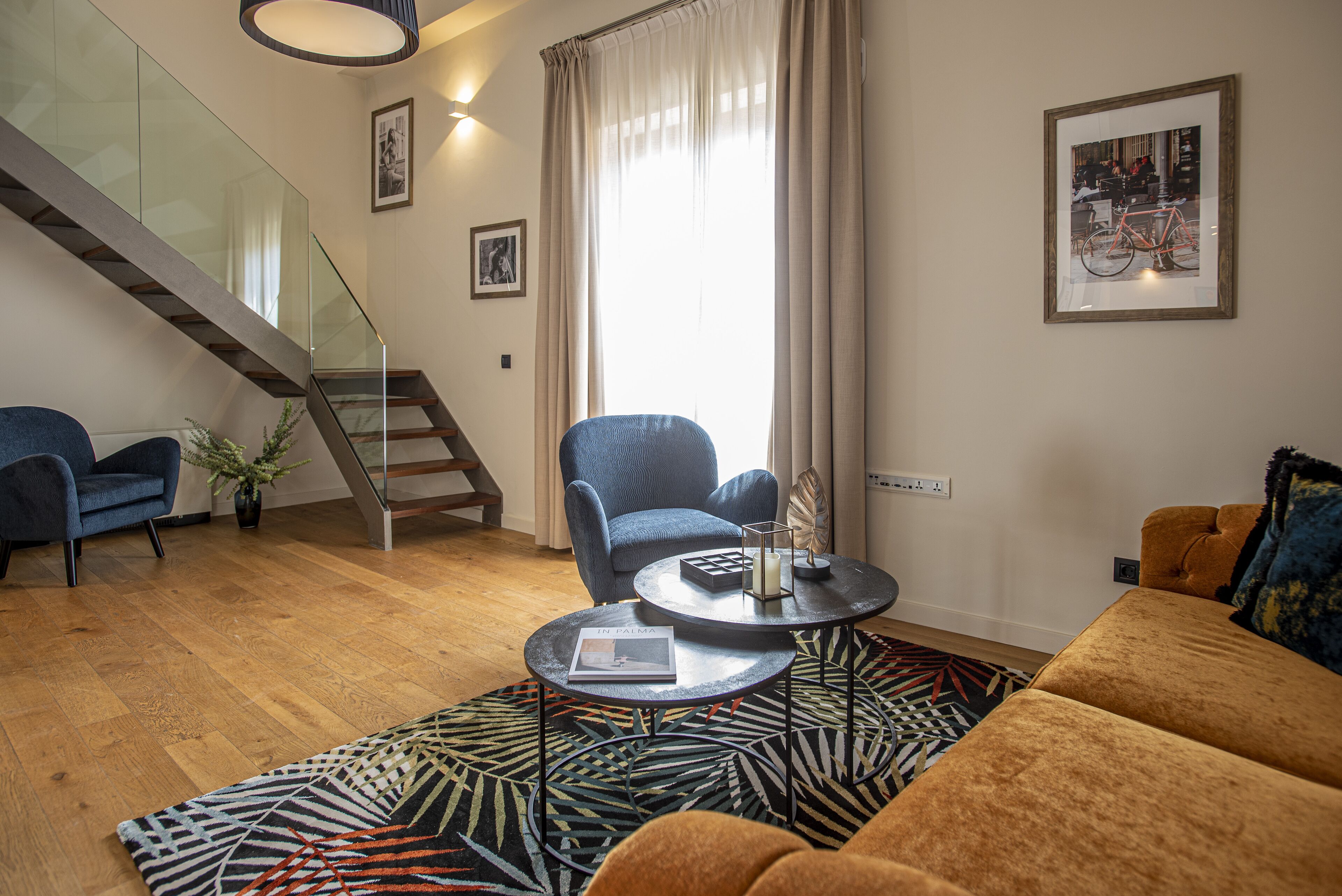 Una sala de estar moderna con una escalera, un sillón azul, una mesa de centro redonda y una alfombra estampada.