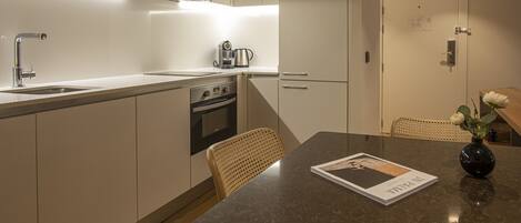 A modern kitchen with a built-in oven, a coffee maker, and a dining area with a table and chairs.