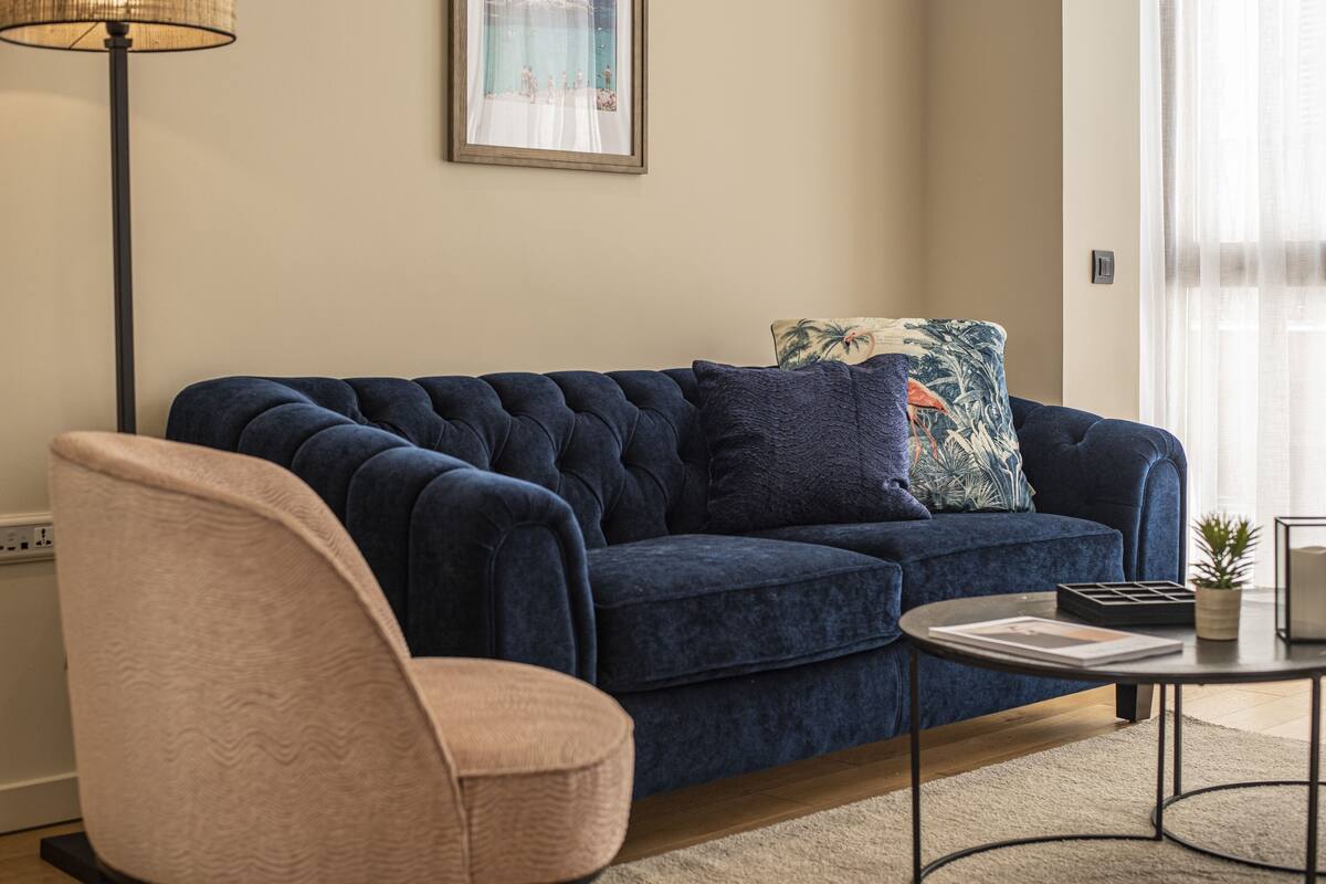 Ein Wohnzimmer mit einem dunkelblauen Sofa, einem hellrosa Sessel, einem kleinen runden Tisch und einer Stehlampe.