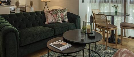 A modern living room with a dark green sofa, a round coffee table, and a dining area with a glass table and wicker chairs.
