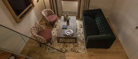 Una sala moderna con una escalera, un sofá verde, dos sillones estampados, una mesa de centro con libros y un televisor fijado a la pared.