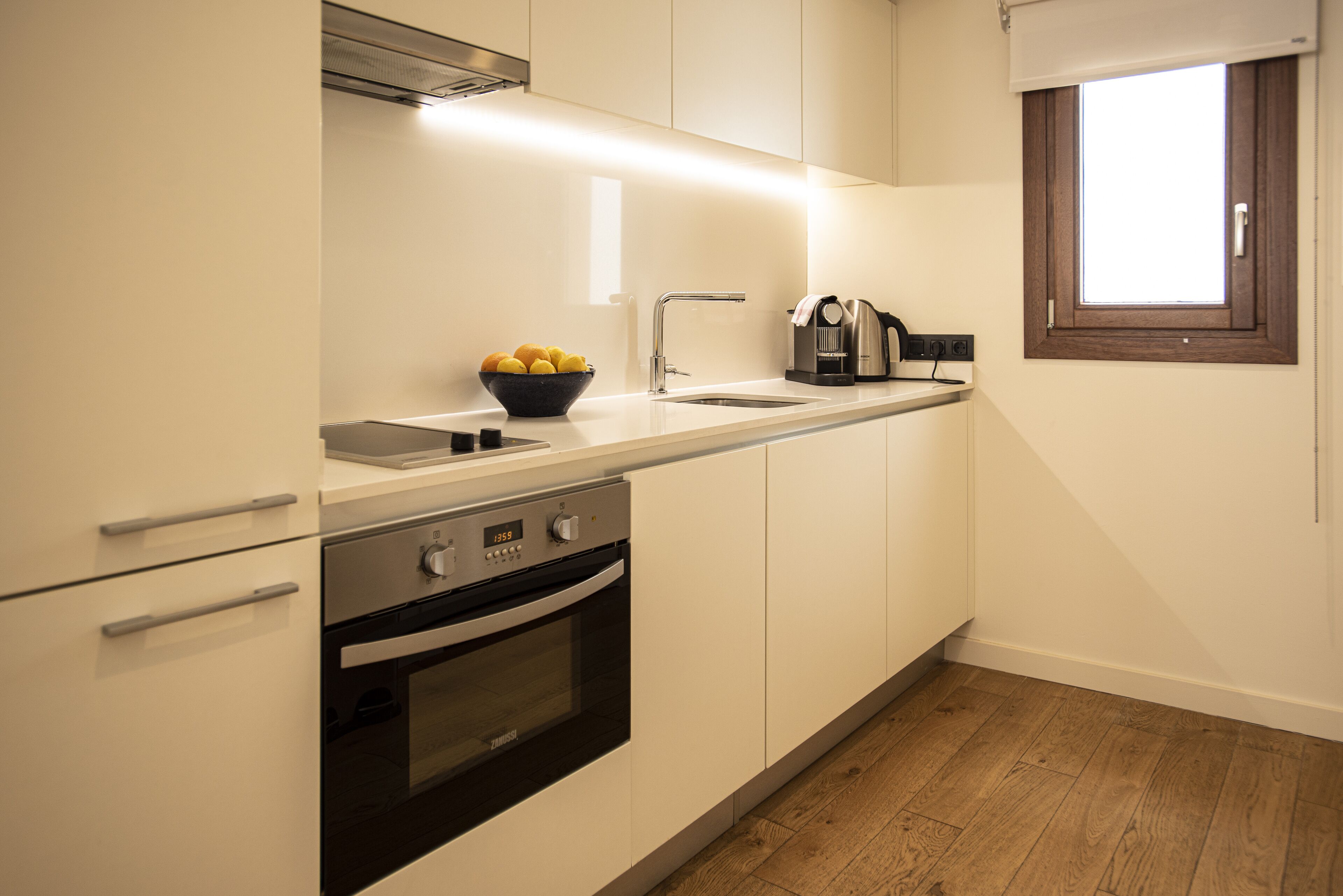 A modern kitchen with white cabinets, a stainless steel oven, a sink, and a window.