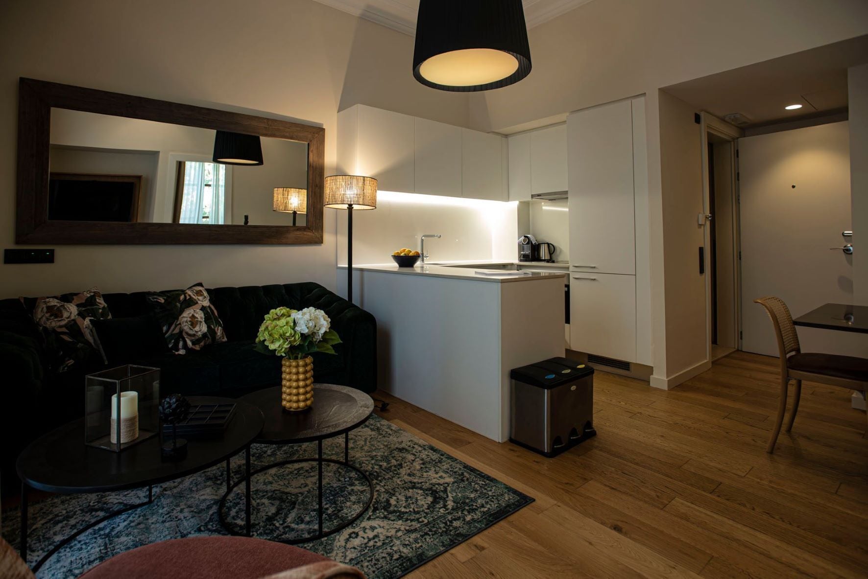 A compact living space with a sofa, coffee table, and a small rug. A kitchenette is visible with a sink and stove.