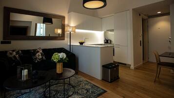 A compact living space with a sofa, coffee table, and a small rug. A kitchenette is visible with a sink and stove.