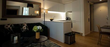 A compact living space with a sofa, coffee table, and a small rug. A kitchenette is visible with a sink and stove.