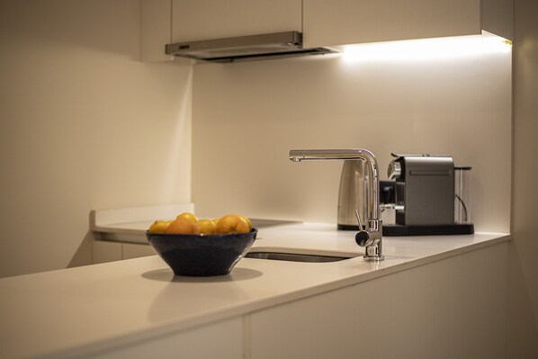 A modern kitchen with a white countertop, a stainless steel sink, and a bowl of fruit.