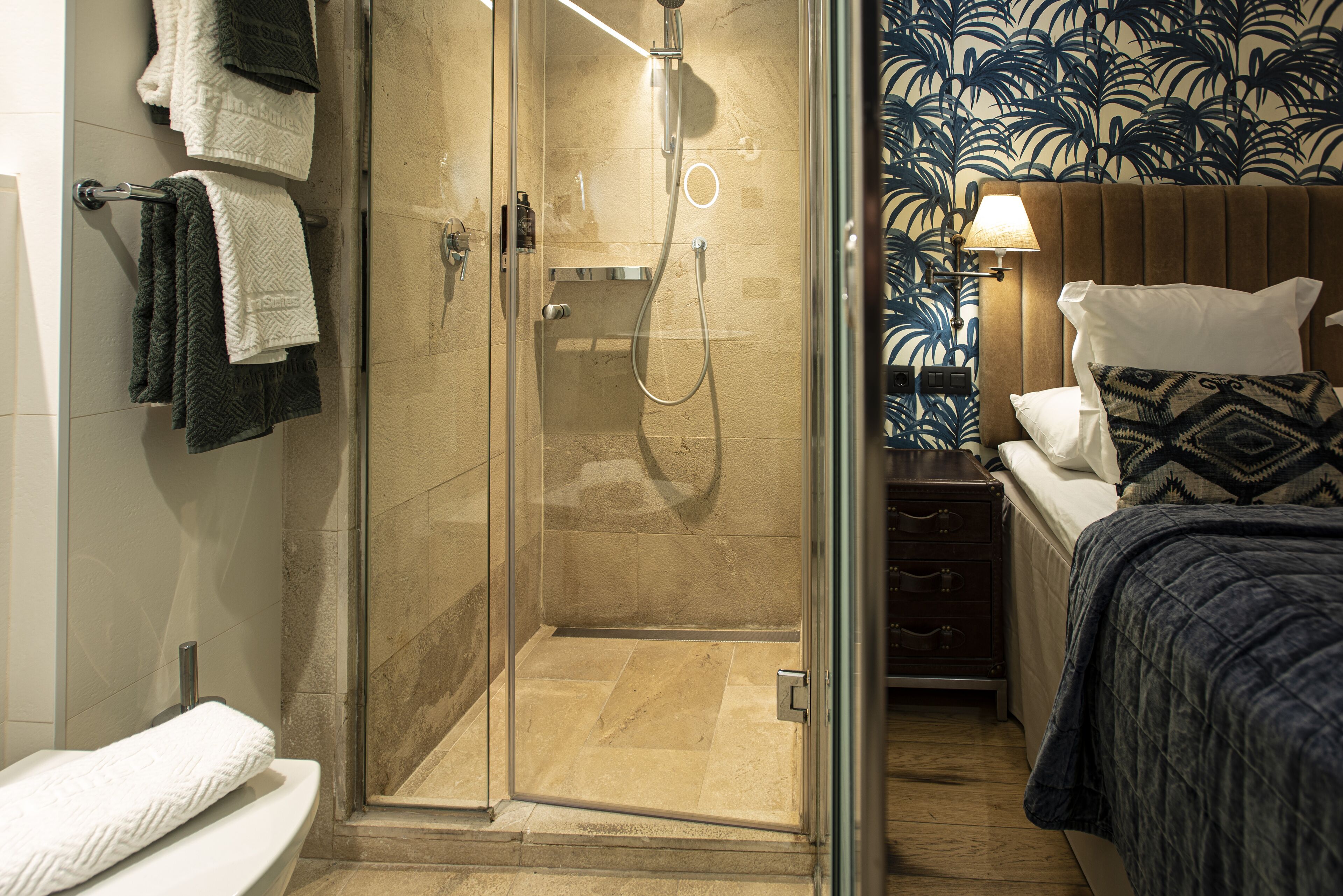 Une salle de bain d’hôtel avec une douche à parois de verre, des toilettes et un lit doté d’une tête de lit à motifs.
