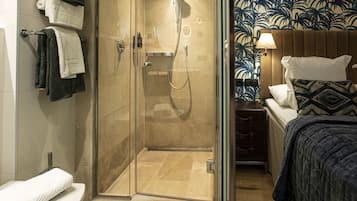 Ein Badezimmer mit Glasdusche, Toilette und einem Bett mit gemustertem Kopfteil.